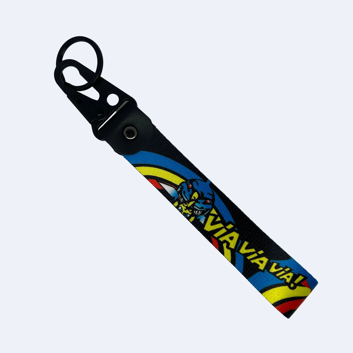 A black fabric keychain or bag strap with a black metal key ring and snap closure, featuring a colorful printed design with the word 'VIA VIA' in yellow and red, a blue monster face, and curved blue, yellow, and red stripes on a light gray background.