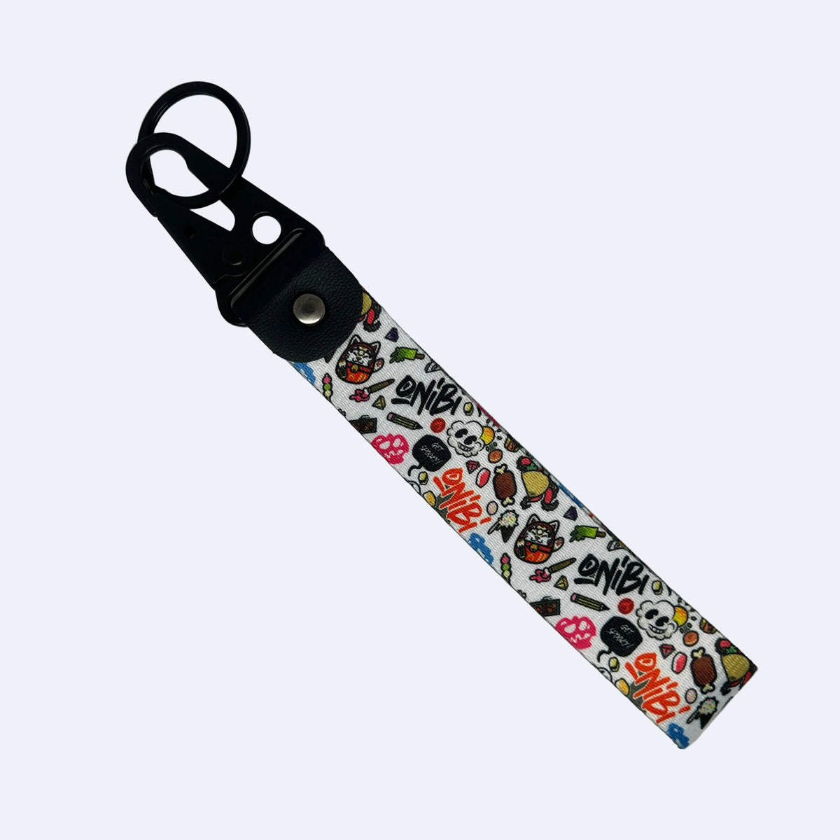 A fabric wrist strap keychain featuring a white background covered in a colorful cartoon and graffiti-style pattern, attached to a black plastic swivel clasp with a metal snap button.