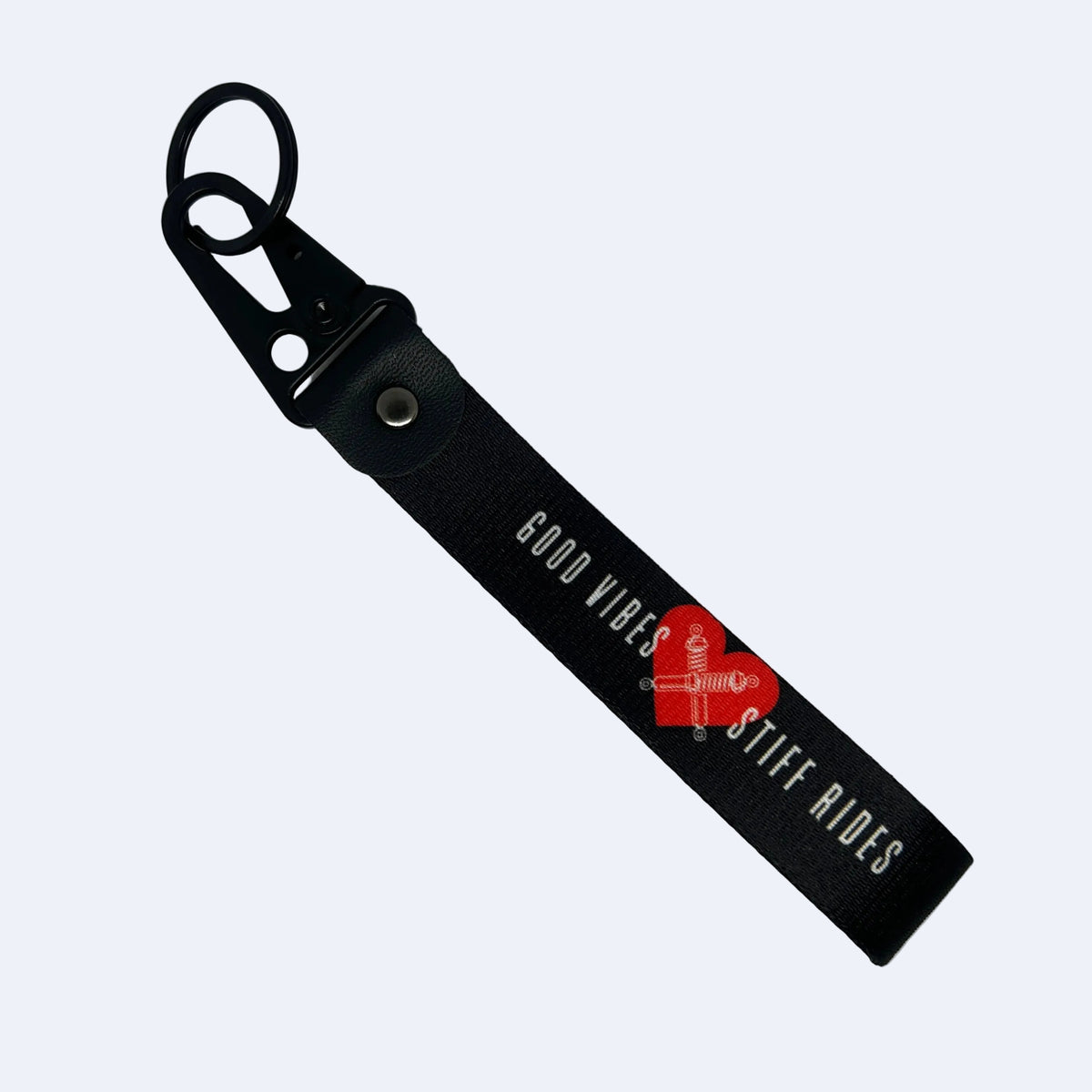A black leather keychain strap with a black metal carabiner clip, featuring the text 'GOOD VIBES STIFF RIDES' in white. A red heart-shaped watermark is overlaid on the center of the strap.