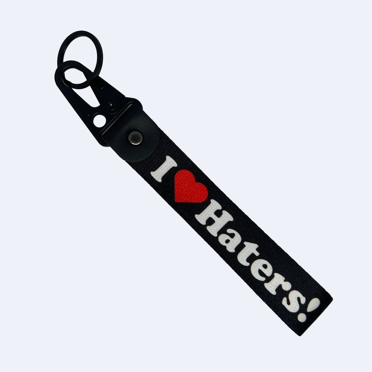 A black fabric keychain strap with a metal clasp and key ring, featuring the text 'I [red heart] Haters!' in white and red, photographed on a light gray background.