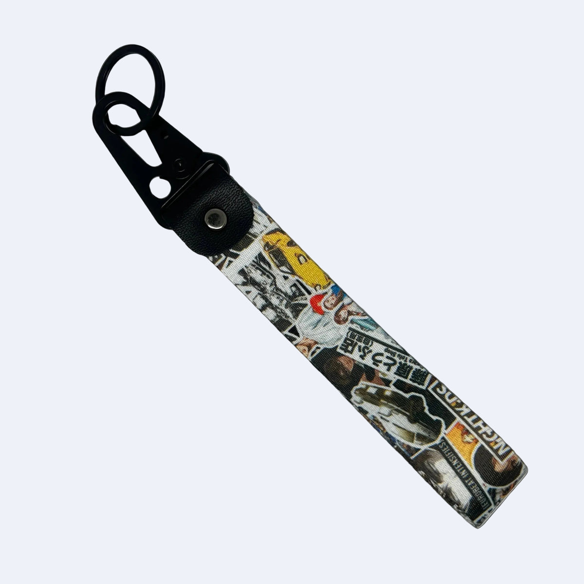 A keychain or bag charm with a black plastic swivel clasp and a fabric strap featuring a busy collage print of stickers, text, and graphics on a light gray background.