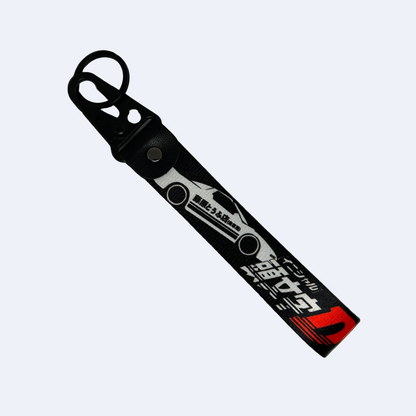 Motorev Initial D AE86 Trueno car key tag, a black wrist strap JDM keyring featuring the iconic Toyota AE86 Trueno silhouette with Japanese kanji and Initial D branding, built for JDM and anime car culture enthusiasts UK
